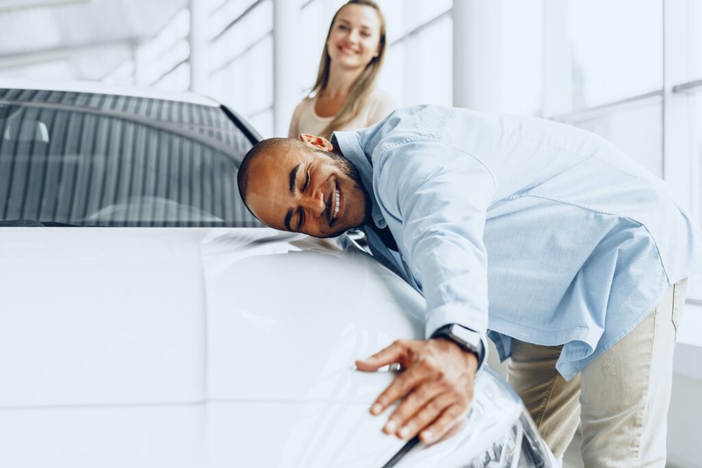 Young couple man and woman hugging their new car in a car shop