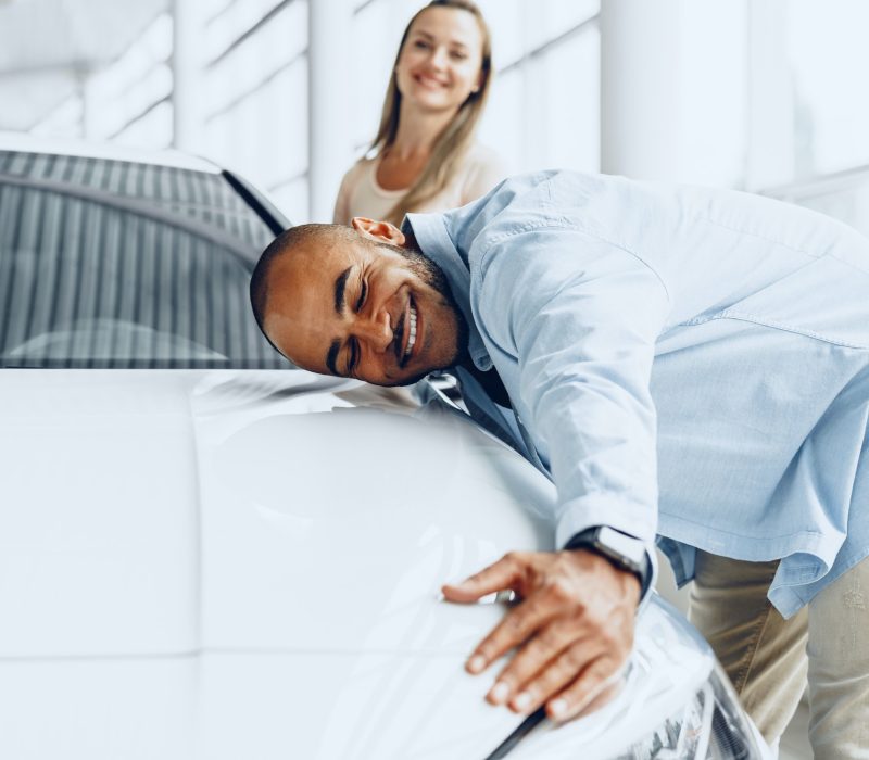 Young couple man and woman hugging their new car in a car shop